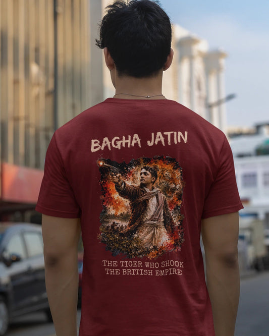 A man viewed from behind wearing a maroon t-shirt with a large graphic print on the back that reads 'BAGHA JATIN' and 'THE TRIN AND HUNGER THE BATTLE EAGLE'. He is standing on a city street with buildings and a car blurred in the background.