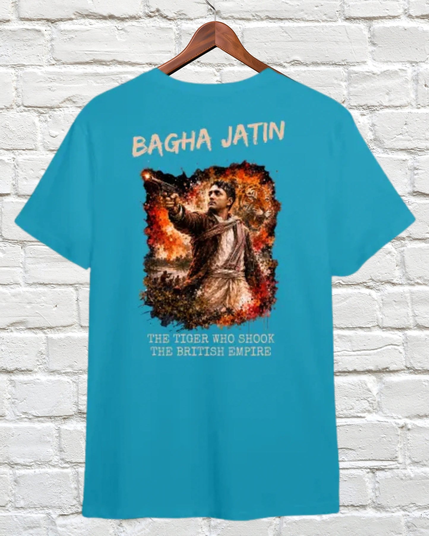 A turquoise blue t-shirt hanging on a wooden hanger against a white brick wall. The back of the shirt features a large graphic print of a historical figure on fire with the text 'BAGHA JATIN' above and 'THE TIMES BIG BOOK THE BRITISH EMPIRE' below.