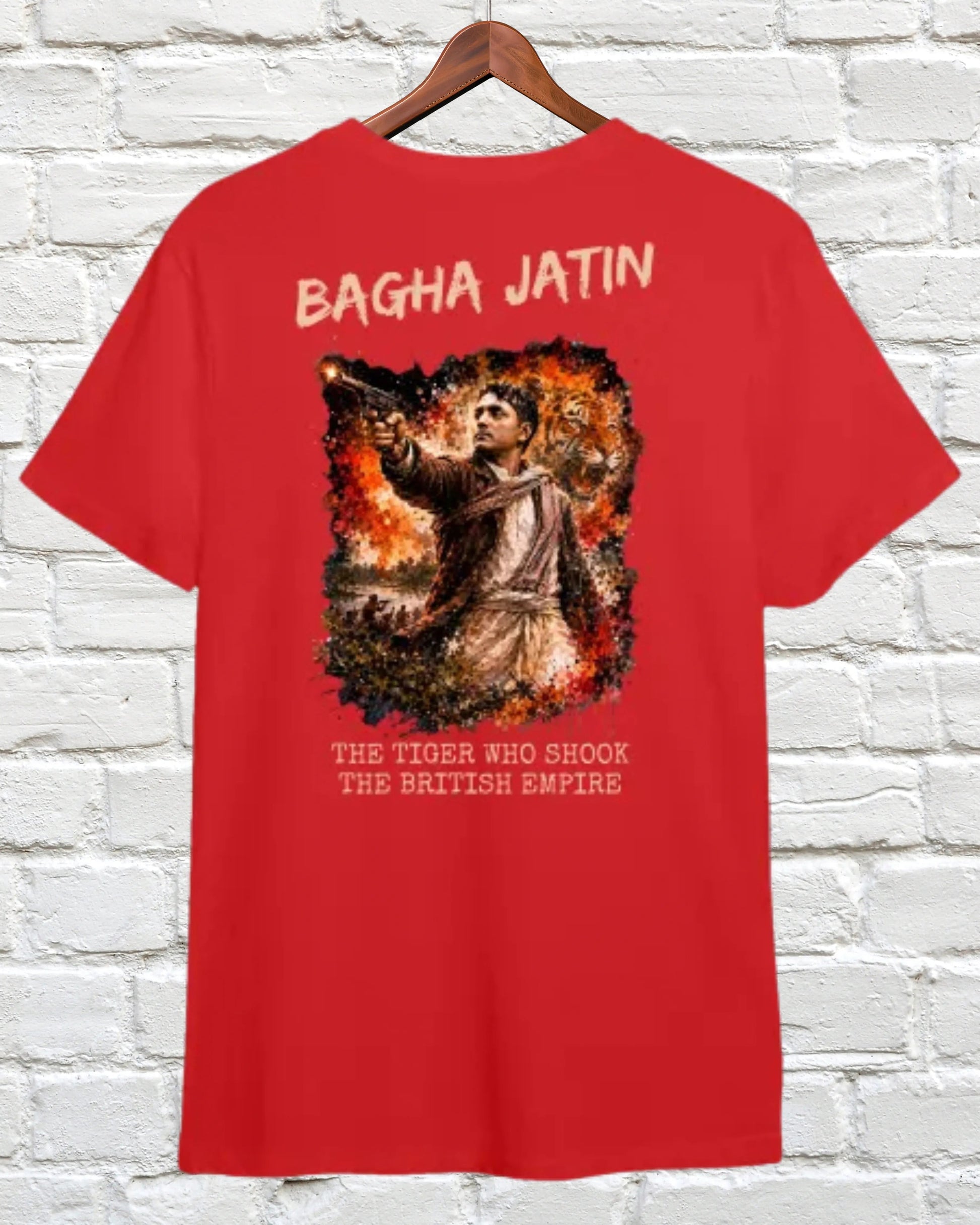 A red short-sleeve t-shirt hanging on a wooden hanger against a white brick wall. The back of the shirt features a large graphic print with the text 'BAGHA JATIN' at the top and 'THE TIGERS WHO SHOOK THE MATTER EMPIRE' at the bottom, surrounding an illustration of a tiger in a fiery scene.