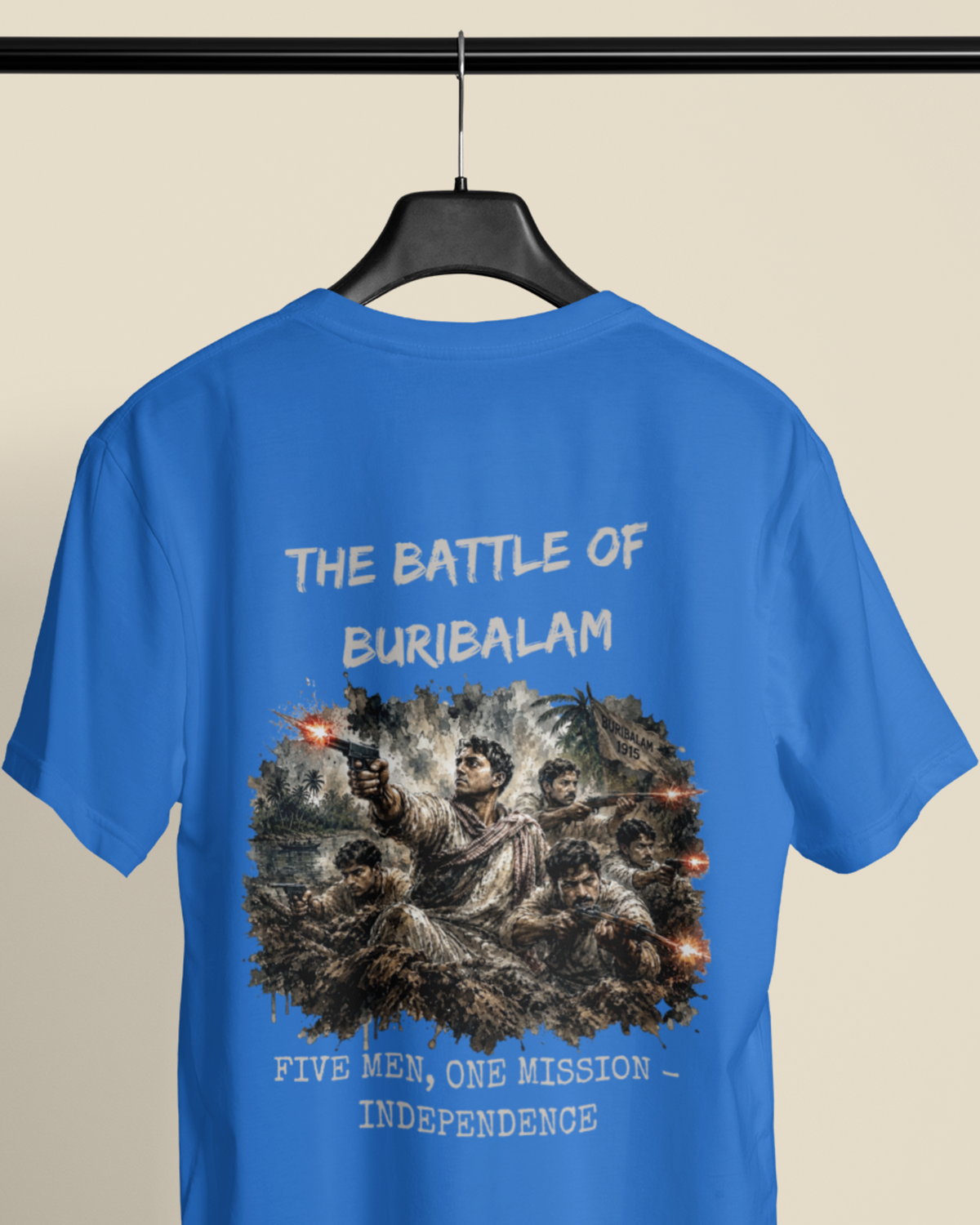A blue short-sleeve t-shirt hanging on a black hanger against a light beige background. The back of the shirt features a large graphic print depicting soldiers in combat with the text 'THE BATTLE OF BURIBALAM' above and 'FIVE MEN, ONE MISSION - INDEPENDENCE' below.