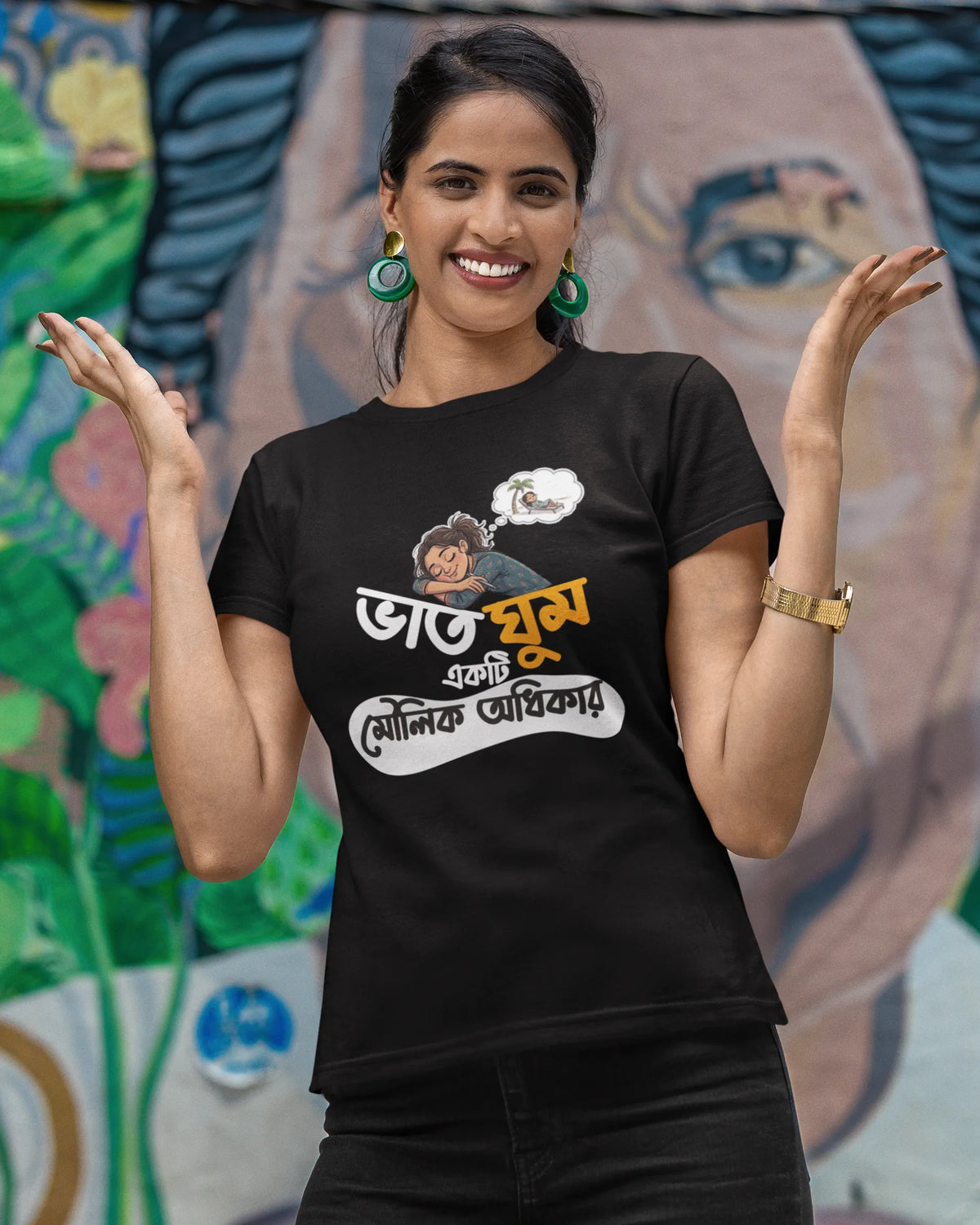 A woman posing in front of a colorful mural wearing a black graphic t-shirt with Bengali text and a cartoon illustration.
