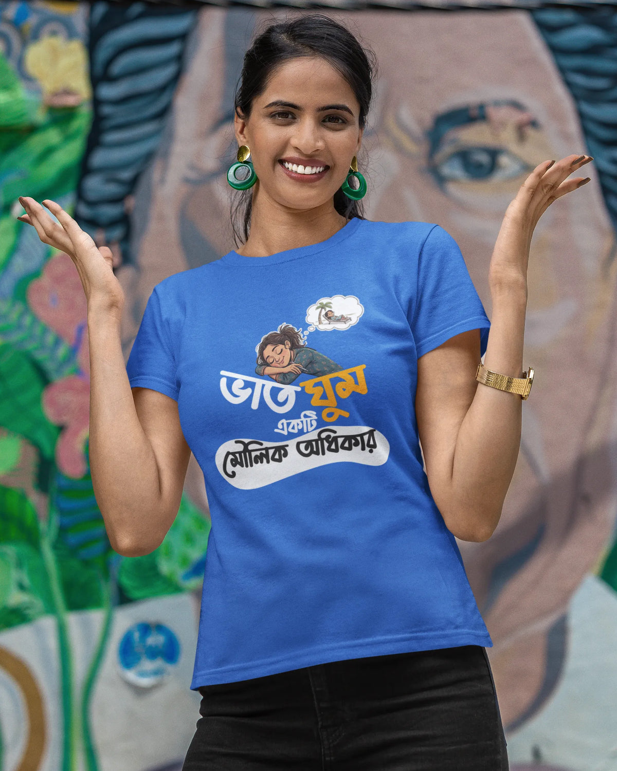 A woman wearing a bright blue graphic t-shirt with Bengali text and a cartoon illustration, posing in front of a colorful painted mural.