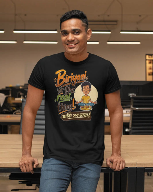 A man standing in a modern office environment wearing a black graphic t-shirt with a colorful print and blue jeans.