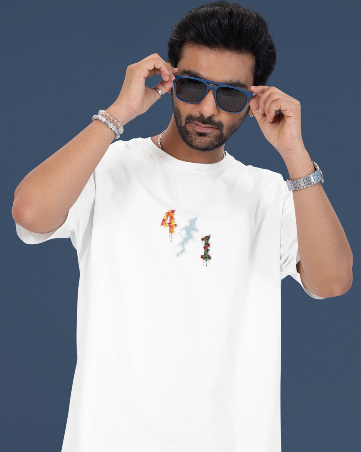 A man wearing a white short-sleeve t-shirt with a small colorful graphic on the chest, blue jeans, and sunglasses, posing against a dark blue background.