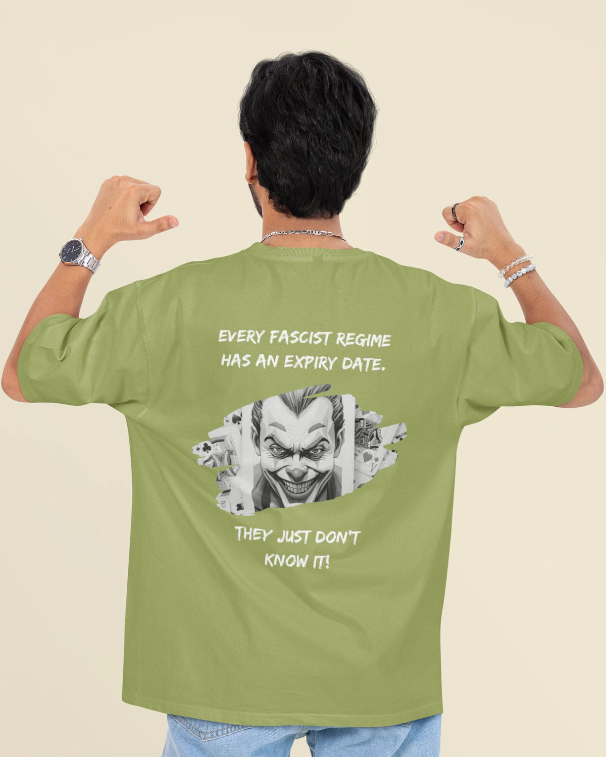 A man shown from behind wearing an olive green t-shirt with a graphic print of the Joker and the text 'EVERY FASCIST REGIME HAS AN EXPIRY DATE. THEY JUST DON'T KNOW IT!'.