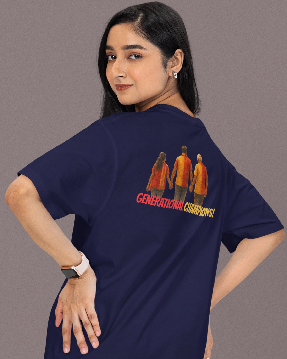 A woman wearing a navy blue t-shirt with a graphic print of three figures and the text 'GENERATIONAL CHAMPIONS' on the back, posed against a solid gray studio background.
