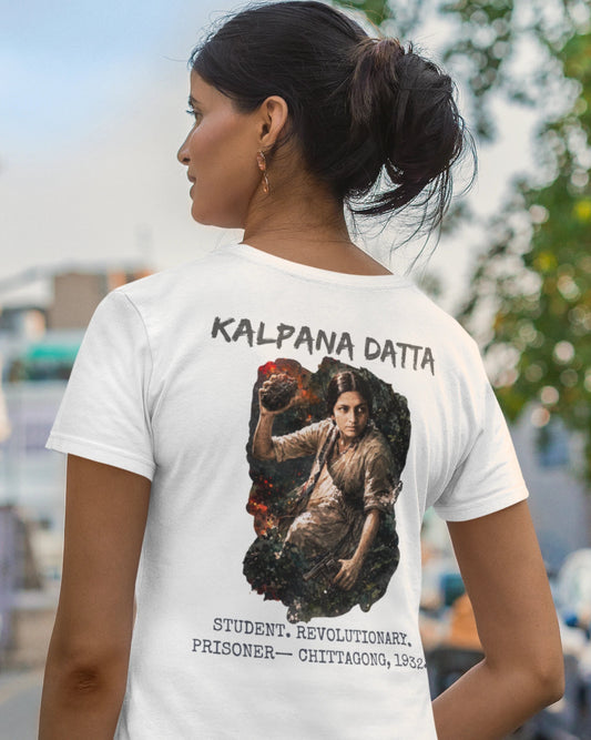A woman shown from the back wearing a white graphic T-shirt with the text 'KALPANA DATTA' and a large printed portrait and additional text on the back, photographed outdoors on a blurred street background.