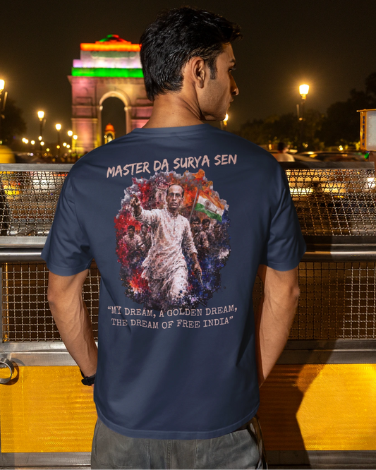 A man stands at night in front of India Gate, wearing a navy blue t-shirt with a large graphic print on the back featuring a portrait of Mahatma Gandhi and the text 'MASTER CA SURYA SEN' and 'WE Dream a GOLDEN dream, THE dream of RAIL BOKS'.
