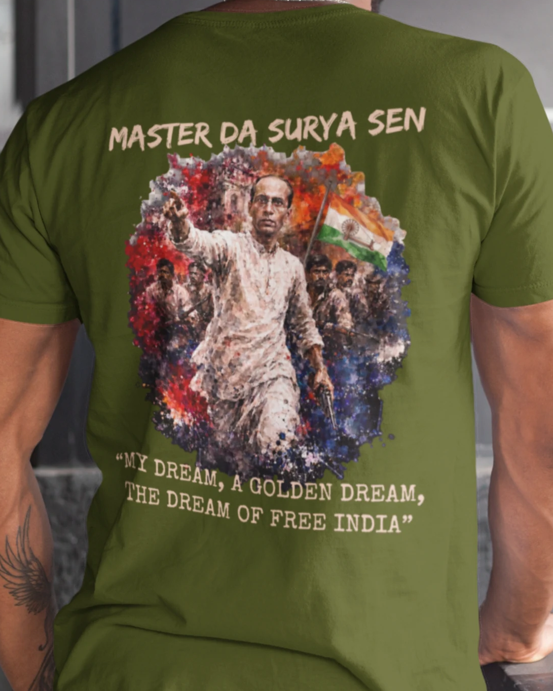 A man viewed from behind wearing an olive green t-shirt with a large graphic print on the back. The graphic features a portrait of Jawaharlal Nehru surrounded by a colorful circular design with the text 'MASTER DA SURYA SEN' at the top and 'MY DREAM, A GOLDEN DREAM, THE DREAM OF FREE INDIA' at the bottom.