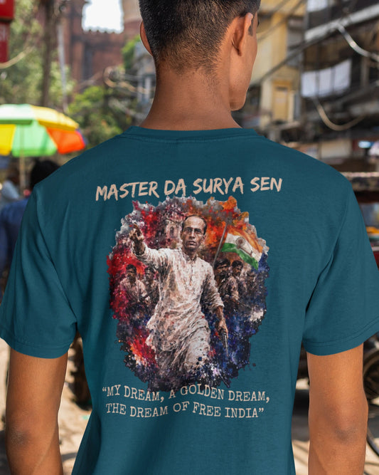A man viewed from behind wearing a teal blue t-shirt with a large graphic print on the back. The graphic features a portrait of Gandhi surrounded by the Indian flag and text reading 'MASTER DA SURYA SEN' and 'MY DREAM, A GOLDEN DREAM, THE DREAM OF FREE INDIA'.