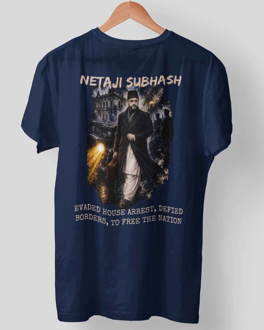 A navy blue short-sleeve t-shirt hanging on a wooden hanger against a light gray background. The back of the shirt features a large graphic print depicting Netaji Subhash with the text 'NETAJI SUBHASH' above and 'EWAGED HOUSE ARREST, DEFIED BORDERS, TO FREE THE NATION' below.