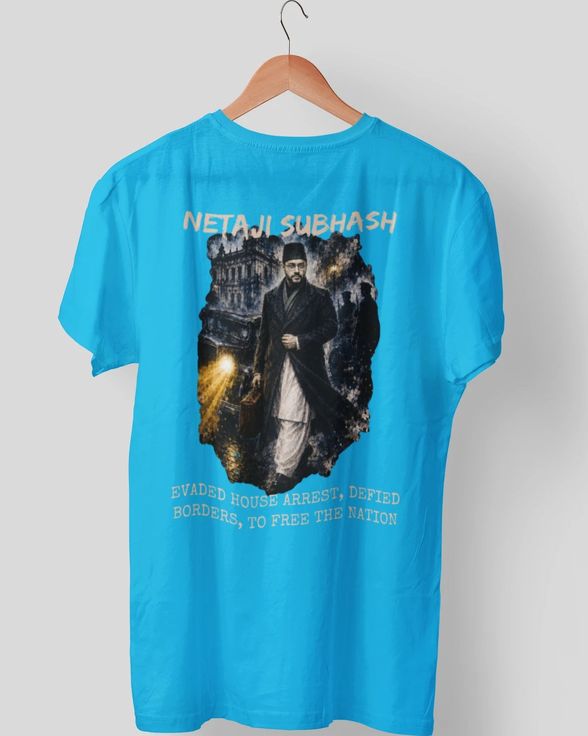 A bright blue short-sleeve t-shirt hanging on a wooden hanger against a light gray background. The back of the shirt features a large graphic print depicting a historical figure in a dark coat, with the text 'NETAJI SUBHASH' above and 'EWAGED HOUSE ARREST / DEPLOYED BORDERS, TO FREE THE NATION' below.