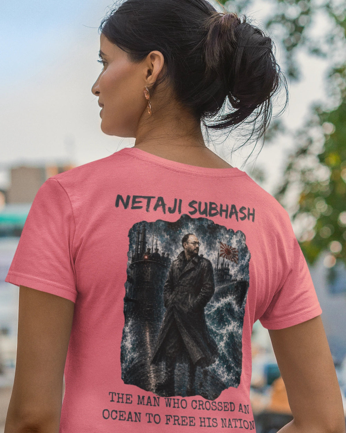 A woman shown from behind wearing a pink graphic t-shirt with a black and white print of a historical figure and text reading 'NETAJI SUBHASH' and 'THE MAN WHO CROSSED AN OCEAN TO FREE HIS NATION'.