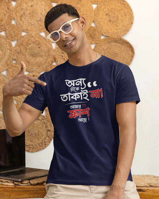 A man wearing a navy blue graphic t-shirt with Bengali text, beige pants, and white-framed sunglasses, posing in front of a wall decorated with circular woven mats.