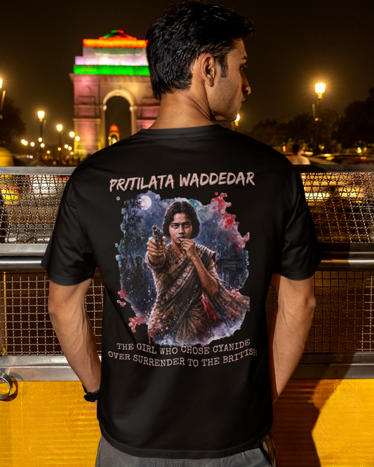 A man stands on a bridge at night with India Gate in the background, wearing a black graphic t-shirt showing a detailed print of a woman with the text 'PRITILATA WADDEDAR'.