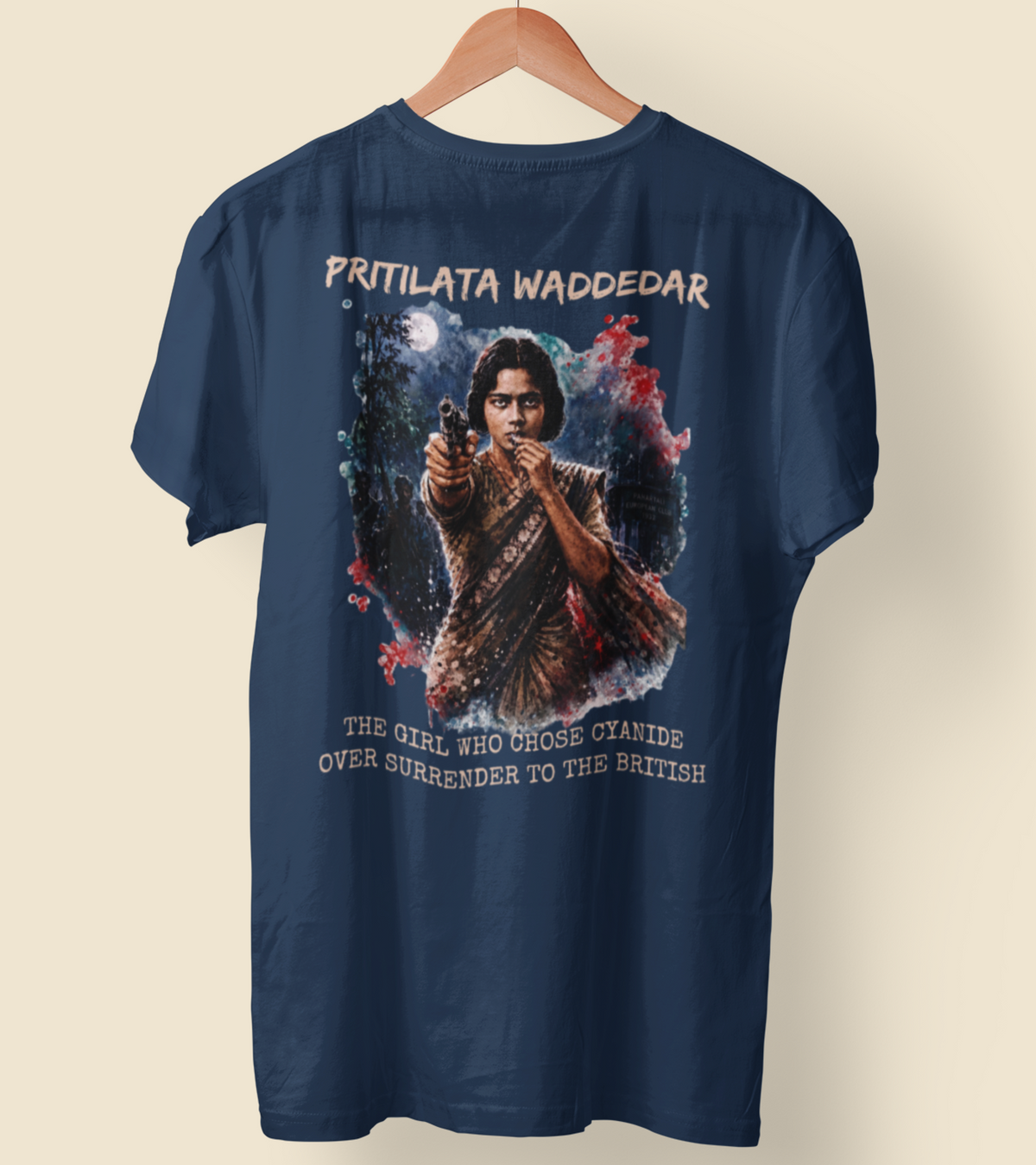 A navy blue short-sleeve t-shirt hanging on a wooden hanger against a light beige background. The back of the shirt features a large graphic print of a woman holding a gun, surrounded by red and white smoke, with the text 'PRITILATA WADDEDAR' at the top and 'THE GIRL WHO CHOSE CYANIDE OVER SURRENDER TO THE BRITISH' at the bottom.
