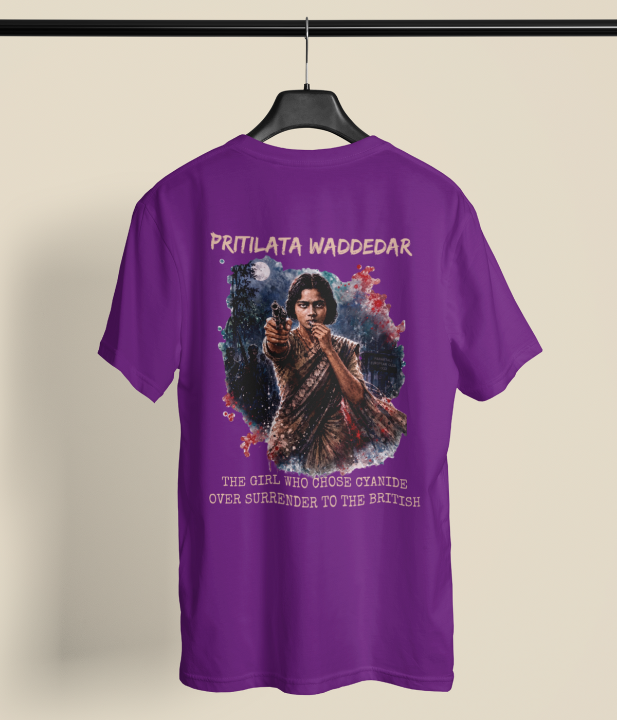 A purple short-sleeve graphic T-shirt hanging on a black hanger against a light beige background. The back of the shirt features a large printed graphic of a young girl in a school uniform pointing a gun, with the text 'PRITILATA WADDEDAR' above and 'THE GIRL WHO CROSSED STANDS OVER SURRENDER TO THE BRITISH' below.