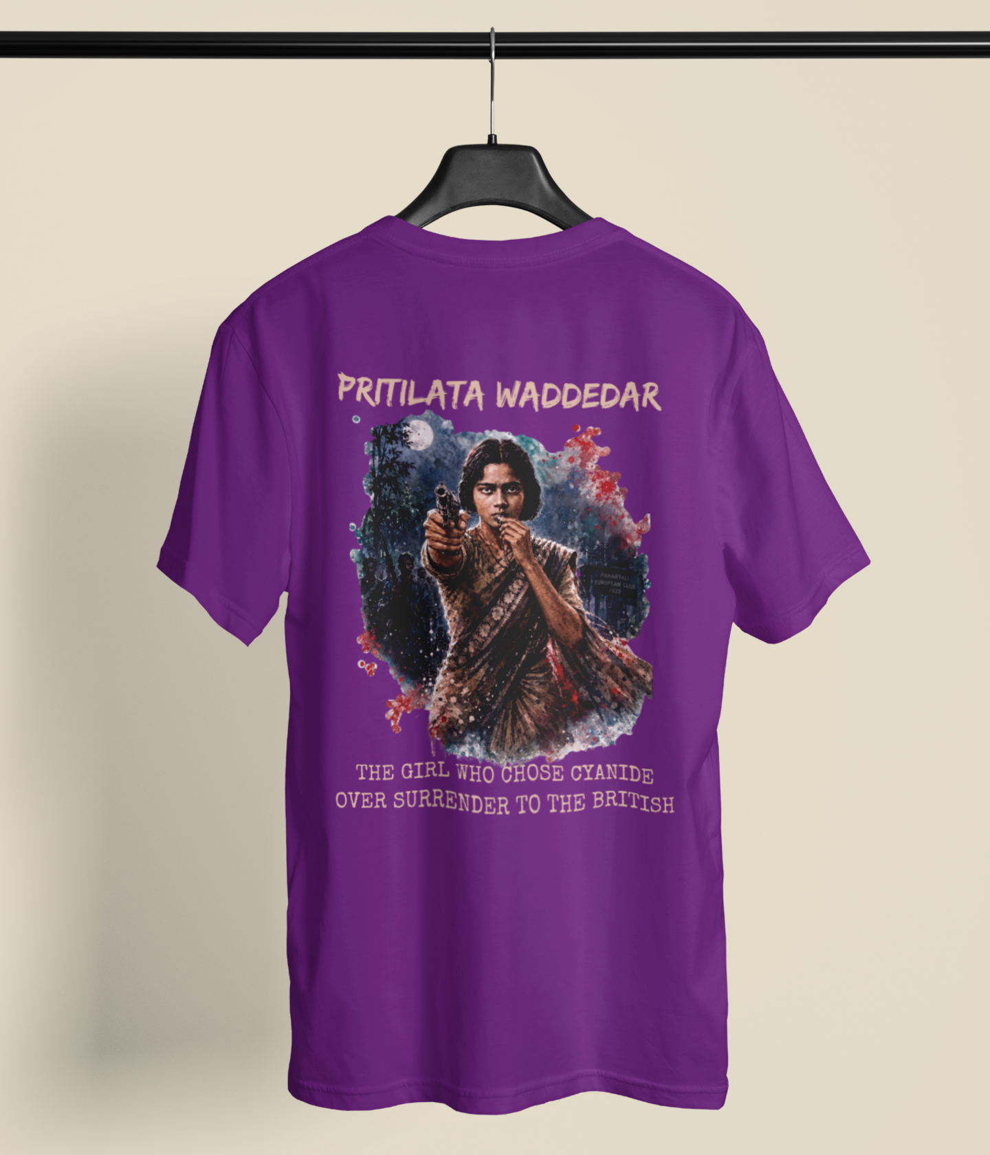 A purple short-sleeve graphic T-shirt hanging on a black hanger against a light beige background. The back of the shirt features a large printed graphic of a young girl in a school uniform pointing a gun, with the text 'PRITILATA WADDEDAR' above and 'THE GIRL WHO CROSSED STANDS OVER SURRENDER TO THE BRITISH' below.